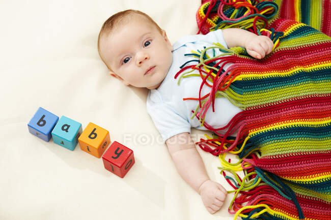 Baby boy lying under striped blanket with blocks spelling baby — Stock Photo