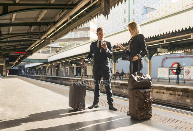 Empresario y mujer de negocios mensajes de texto en la plataforma, Estación de metro, Londres, Reino Unido - foto de stock