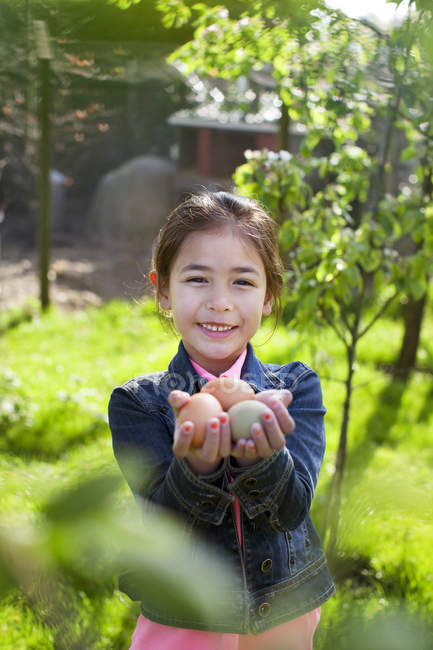 Chica joven sosteniendo huevos en el jardín - foto de stock