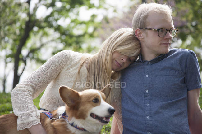 Young couple sitting in park with corgi dog — Stock Photo