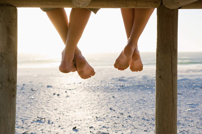 Cropped image of friends sitting barefoot on pier — Stock Photo