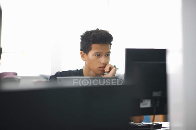 Joven estudiante universitario en la computadora de lectura de escritorio - foto de stock