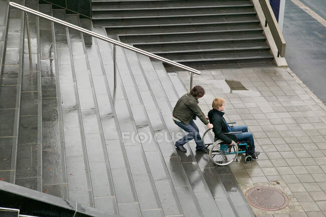 Man helping disabled person up stairway — Stock Photo