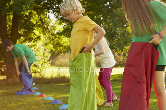 Chicas y niños preparándose para la carrera de sacos en la línea de salida en el parque - foto de stock