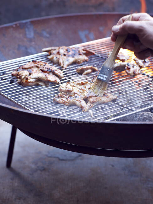 Mans hand painting cooking oil onto quail breast on barbecue — Stock Photo