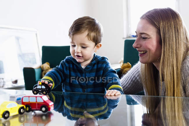 Взрослая женщина и маленький сын играют с игрушечными машинами на столе — стоковое фото