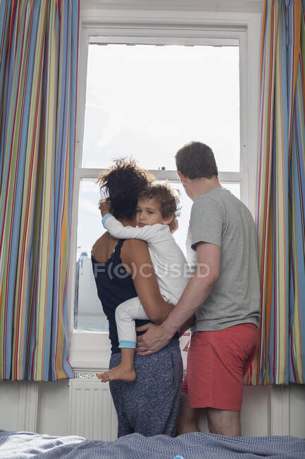 Familia joven mirando por la ventana, vista trasera - foto de stock