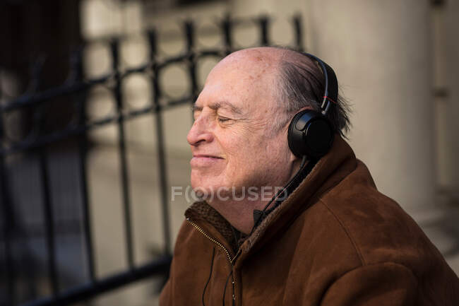 Hombre mayor con los ojos cerrados usando auriculares - foto de stock