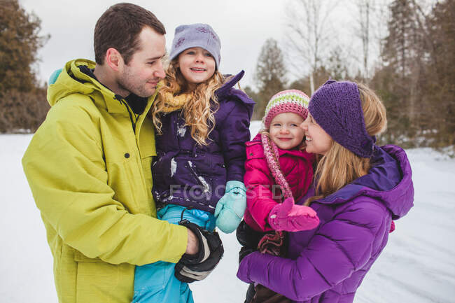 Madre y padre llevando hijas en la nieve - foto de stock