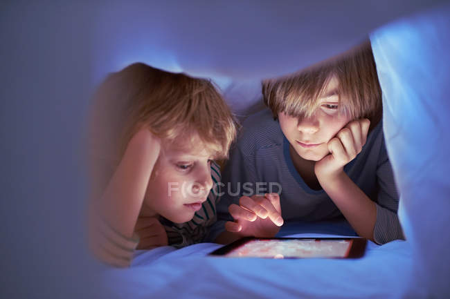 Brothers underneath duvet using digital tablet — Stock Photo