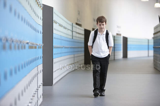 Colegial infeliz caminando solo en el pasillo escolar - foto de stock