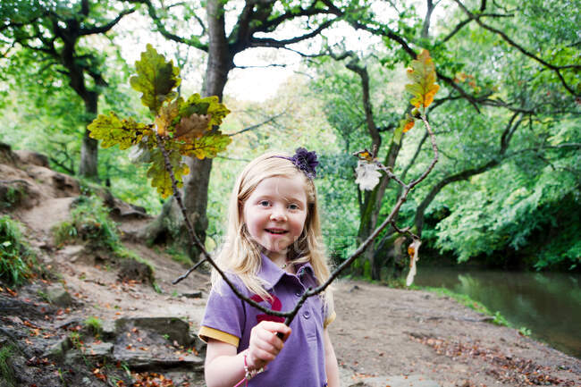 Niña sosteniendo una rama de roble en un bosque - foto de stock