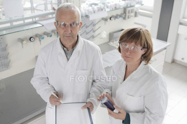 Scientifiques travaillant en laboratoire, tenant du liquide bleu en flacon — Photo de stock