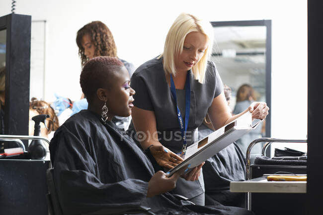 Junge Frau im Friseursalon trägt Haarschnitt-Umhang und wählt Haarfärbefarbe aus Mustern — Stockfoto