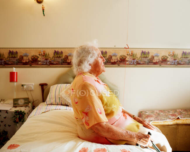 Elderly woman sitting on her bed — Stock Photo