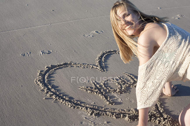 Улыбающиеся женщина, написание сообщение любви в песок, Breezy Point, Квинс, Нью-Йорк, США — стоковое фото