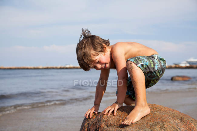 Niño agachado en roca en la playa - foto de stock