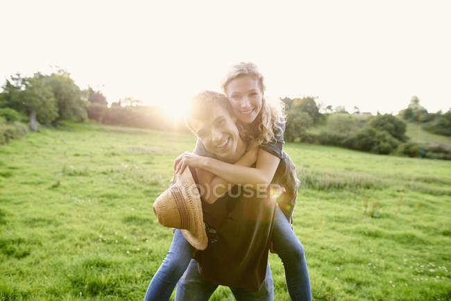 Portrait of young man giving girlfriend a piggyback in rural field — Stock Photo