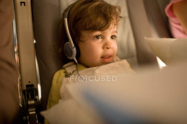 Junges Mädchen sitzt mit Kopfhörern im Flugzeug — Stockfoto