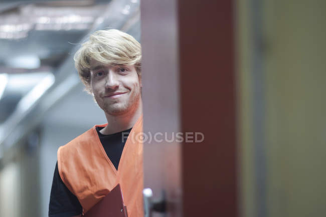 Blick durch die Tür eines jungen Mannes mit Warnweste, der lächelnd in die Kamera blickt — Stockfoto