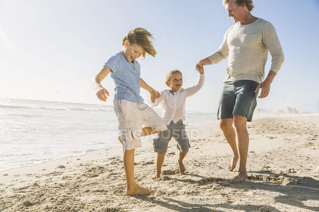 Отец и сыновья на пляже держатся за руки — стоковое фото