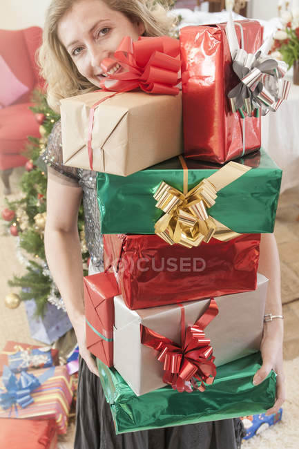 Woman holding stack of christmas gifts looking at camera smiling — Stock Photo