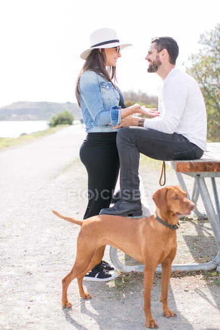 Беременная взрослая пара, обсуждающая на скамейке в парке на побережье — стоковое фото