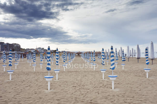 Ряди складених пляжних парасольок під хмарним небом — стокове фото