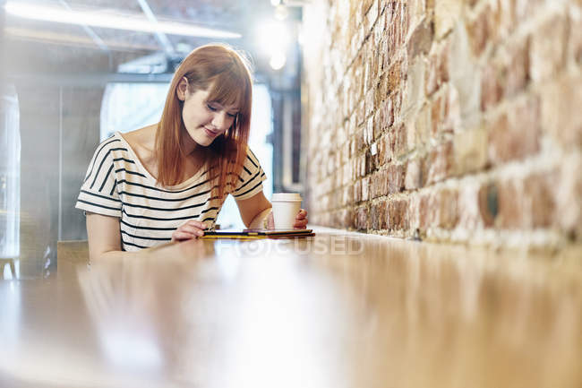 Жінка п'є каву і використовує таблетку в кафе — стокове фото