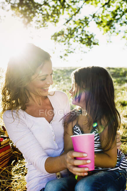 Mujer madura e hija bebiendo de vasos de papel en el picnic del parque - foto de stock