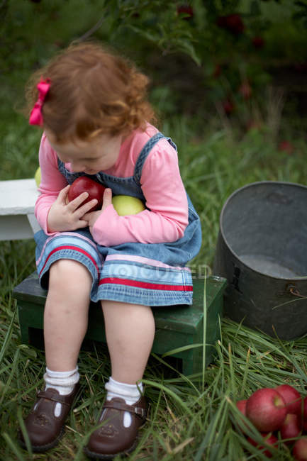 Ragazza seduta sulla panchina con le mele in mano — Foto stock