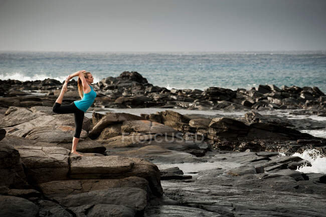 Woman practicing yoga on rock formation — Stock Photo