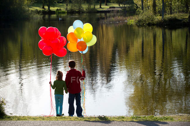 Hermano y hermana frente al lago con manojos de globos - foto de stock