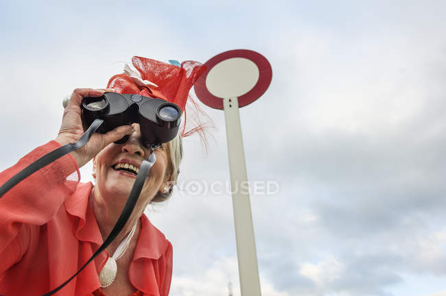 Mujer mayor en carreras inclinadas hacia adelante y mirando a través de prismáticos - foto de stock