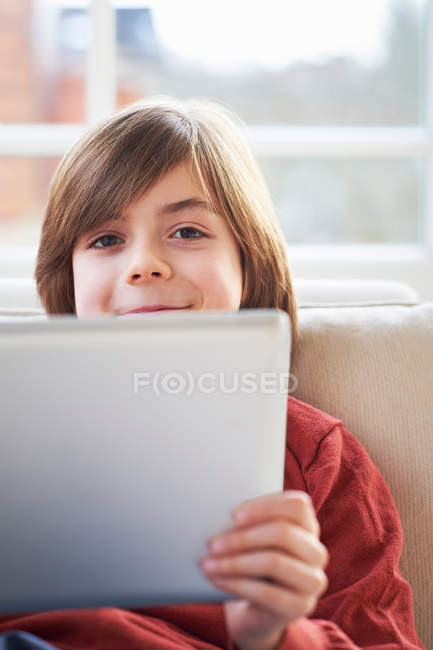 Niño usando tableta digital y sonriendo a la cámara - foto de stock