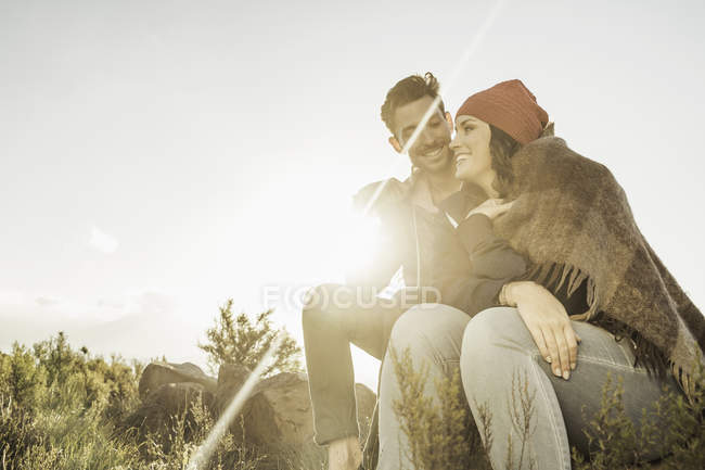 Couple wrapped in blanket sitting on rock in field — Stock Photo