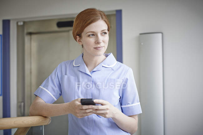 Enfermera con teléfono móvil fuera del ascensor del hospital - foto de stock