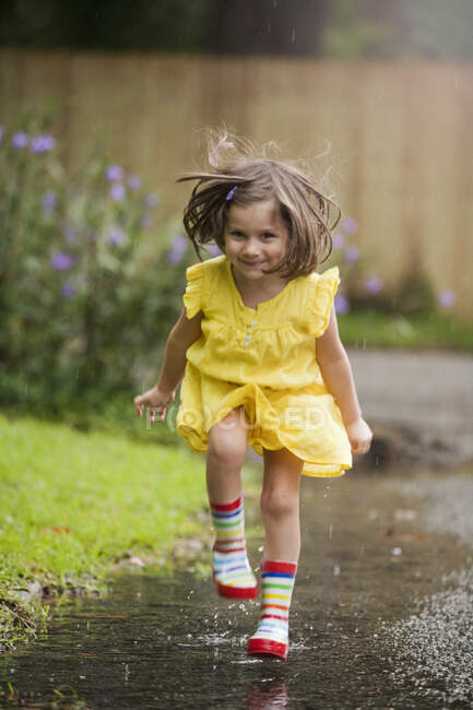 Menina usando botas de borracha correndo na poça de chuva — Fotografia de Stock