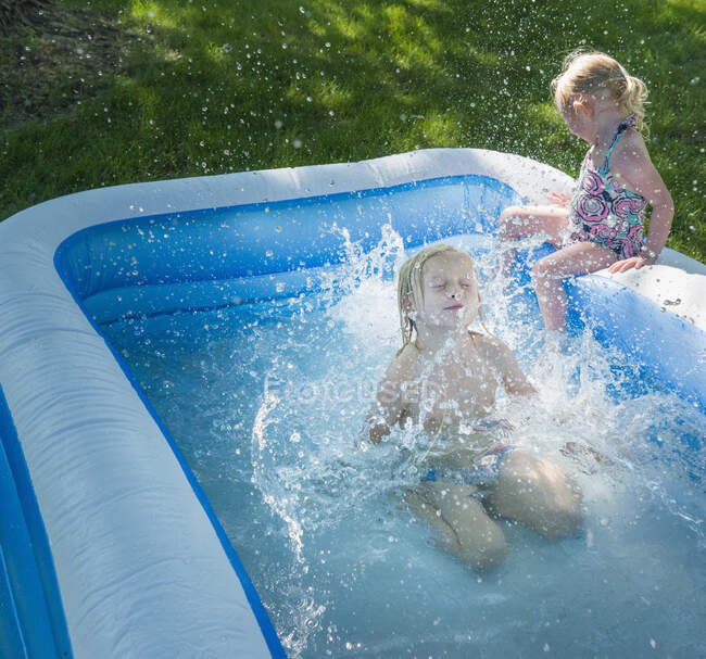 Girl watching big brother jump into paddling pool — Stock Photo