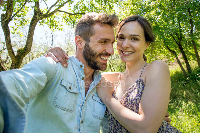 Young woman with arm around young man looking at camera smiling — Stock Photo