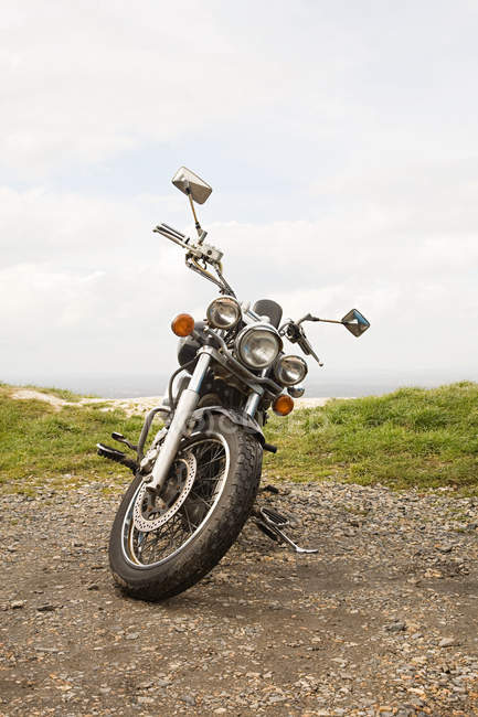 Мотоцикл стоит на сельской дороге с травой в облачный день — стоковое фото
