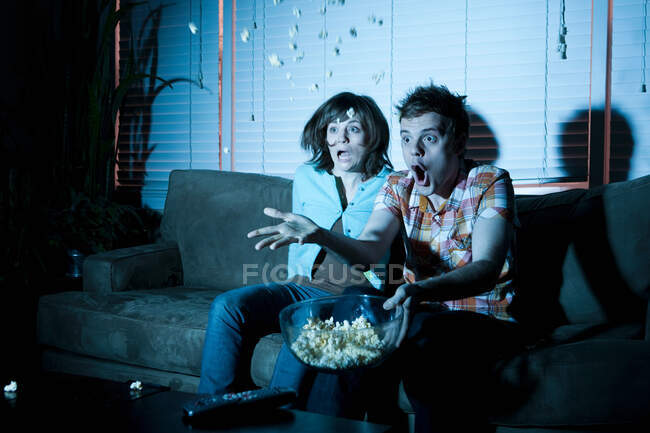 Молодая пара смотрит телевизор, мужчина бросает попкорн — стоковое фото
