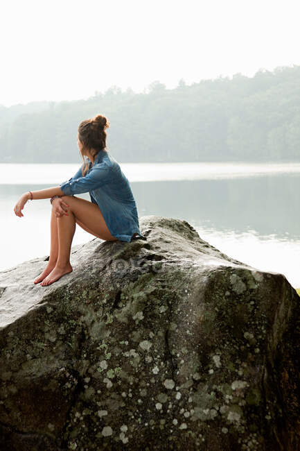 Jovem mulher sentada na rocha com vista para o lago — Fotografia de Stock