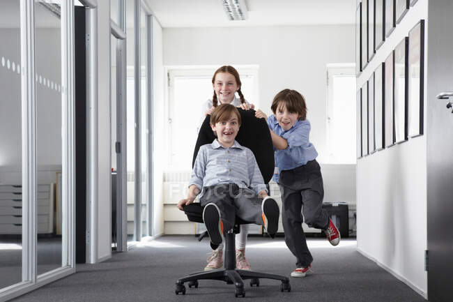 Drei Kinder spielen im Büroflur auf Bürostuhl — Stockfoto