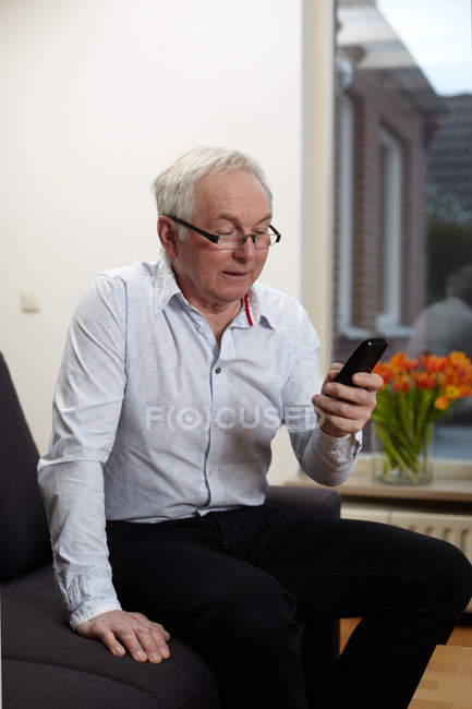 Homem sênior usando smartphone em casa — Fotografia de Stock