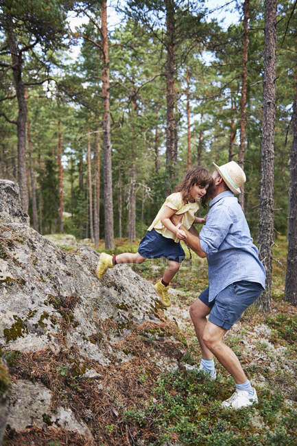 Отец поднимает дочь со скалы — стоковое фото