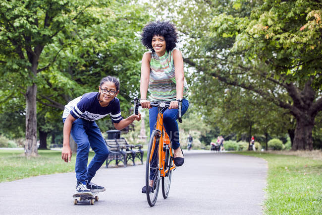 Парень-скейтбордист держит в парке велосипед для матерей — стоковое фото