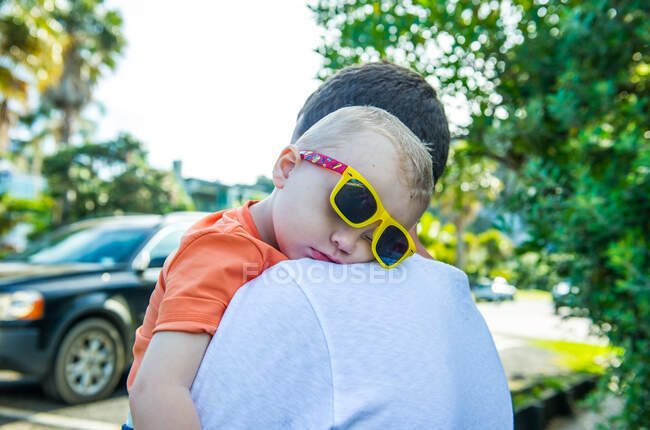 Pai carregando menino dormindo usando óculos escuros amarelos — Fotografia de Stock