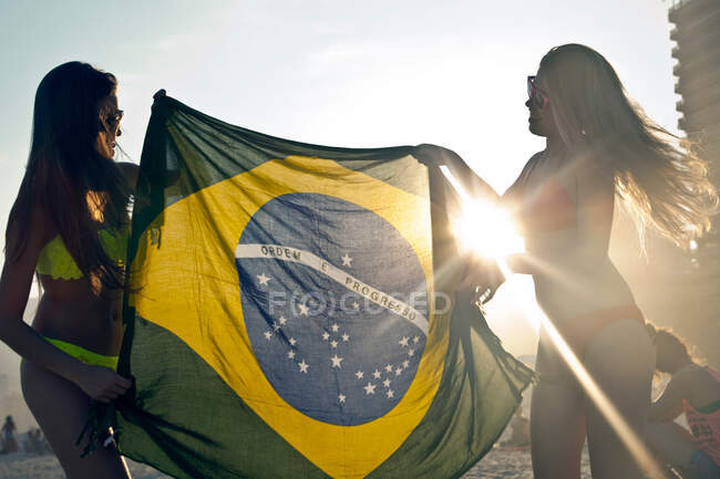 Dos jóvenes con bandera brasileña a la luz del sol - foto de stock