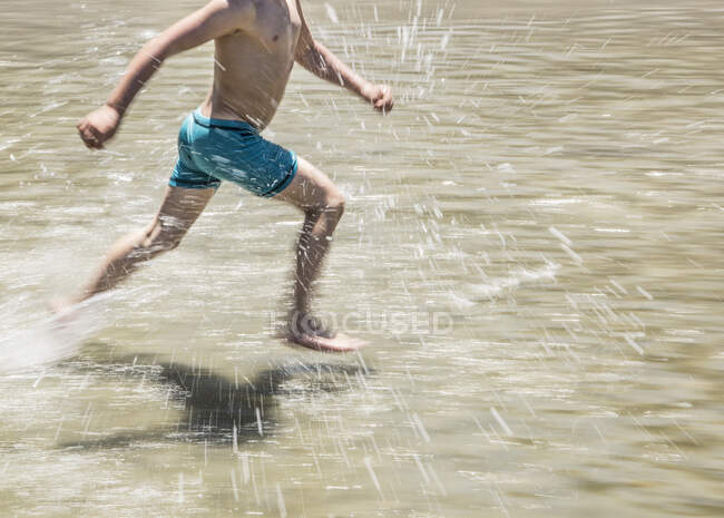 Basse section d'un garçon courant en eau peu profonde — Photo de stock
